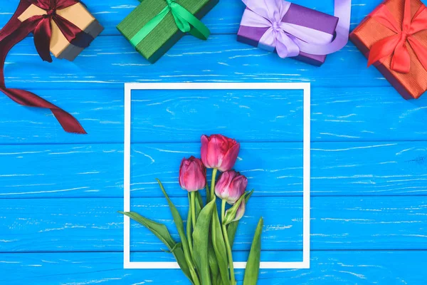 Vue du dessus des coffrets cadeaux et des tulipes roses dans le cadre sur la table bleue — Photo de stock