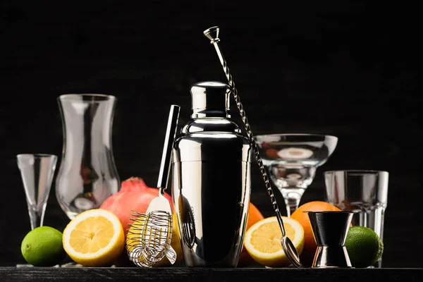 Shaker for preparing alcohol cocktail, empty glasses and fruits on table isolated on black — Stock Photo