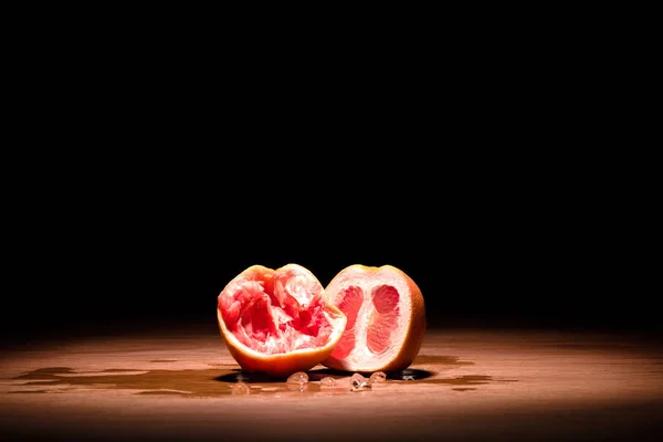 Squeezed and whole halves of grapefruit on wooden table in dark room — Stock Photo