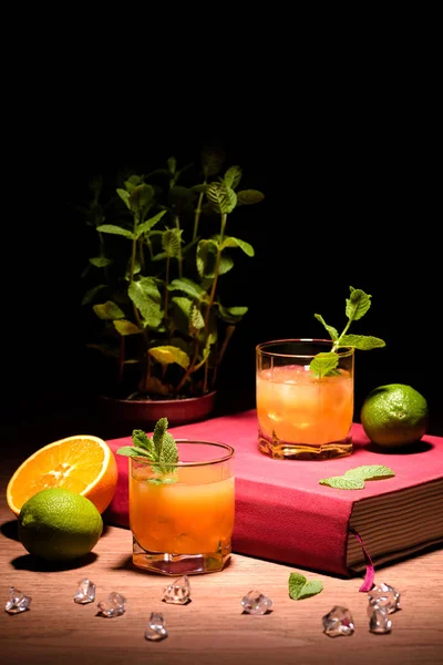 Boissons alcoolisées avec menthe et fruits sur le livre rose sur la table — Photo de stock