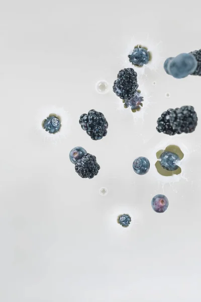 Juicy berries falling into milk on white background — Stock Photo