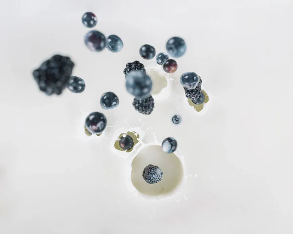 Ripe organic berries falling into milk on white background — Stock Photo