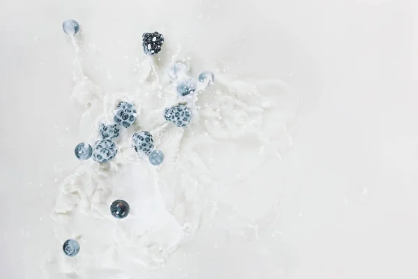 Splashes of milk with raw berries on white background — Stock Photo