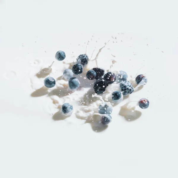Raw berries dropping in milk with splashes on white background — Stock Photo