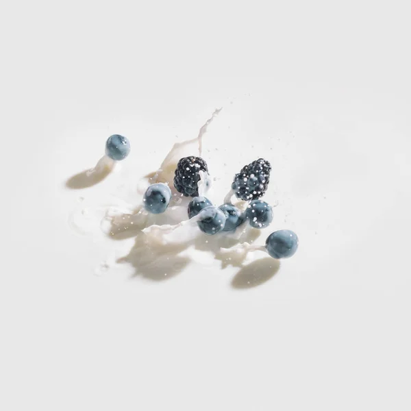 Berries dropping in milk with splashes on white background — Stock Photo