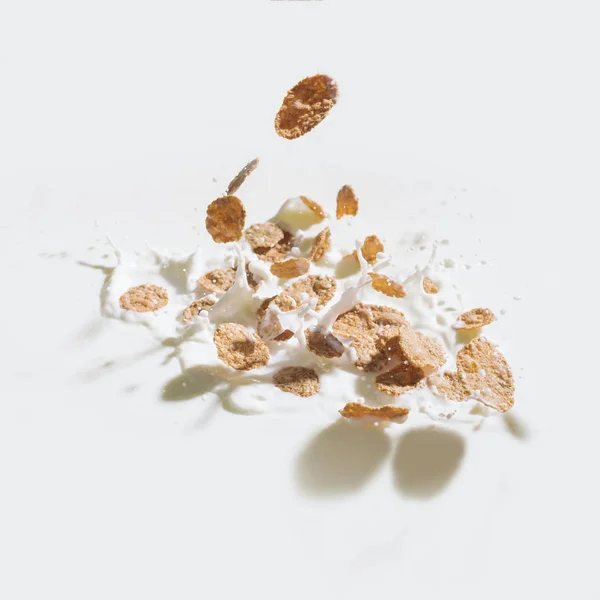 Cornflakes fallen in Milch mit Tropfen auf weißem Hintergrund — Stockfoto