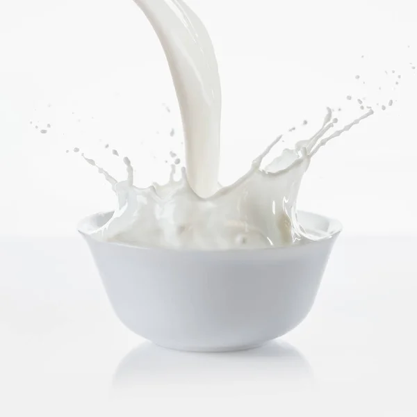 Молоко льется с брызгами в белой миске на белом фоне — стоковое фото