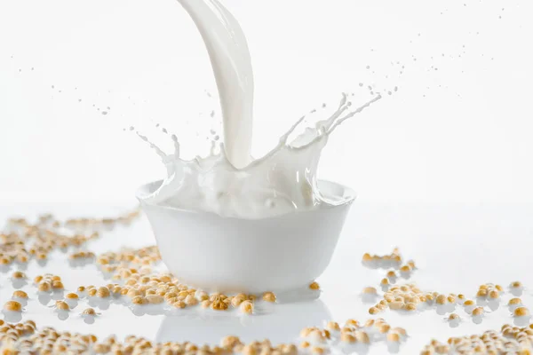 Leche vertiendo en un tazón blanco con soja sobre fondo blanco — Stock Photo