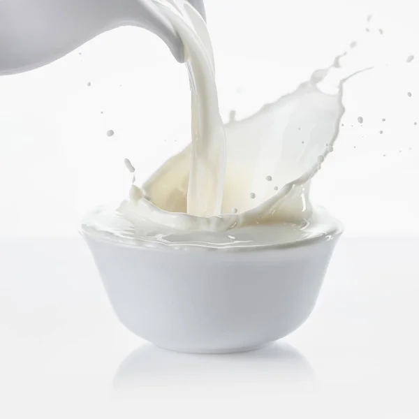 Milch aus Krug in Schüssel auf weißem Hintergrund gießen — Stockfoto
