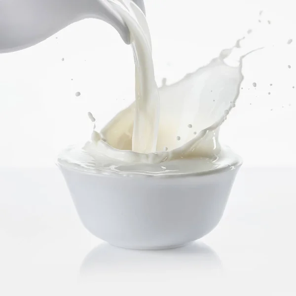 Pouring milk from jug in bowl on white background — Stock Photo