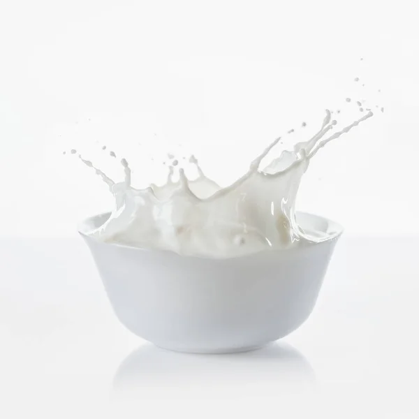 Молоко в білій мисці з краплями на білому тлі — стокове фото