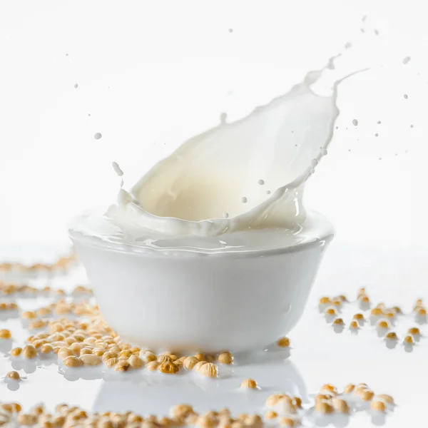 Lait dans un bol blanc avec des gouttes sur du soja sur fond blanc — Photo de stock