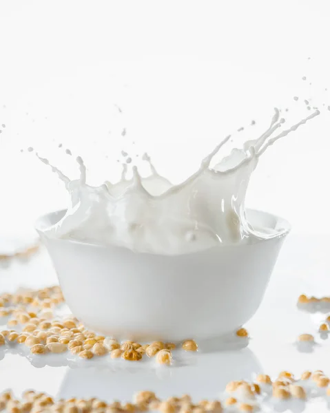 Latte spruzzato in ciotola bianca con semi di soia su fondo bianco — Foto stock