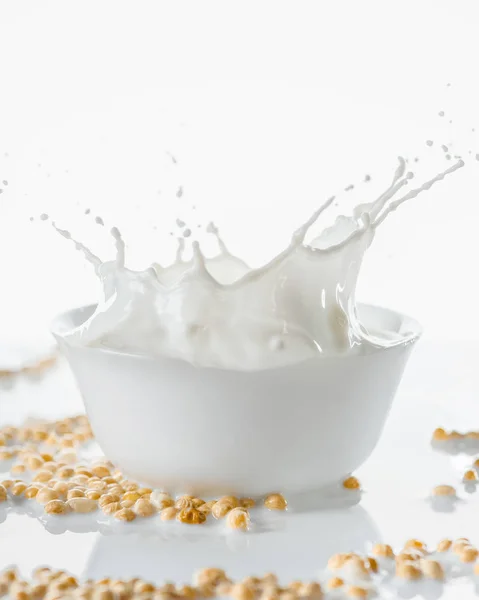 Leche salpicada en tazón blanco con soja sobre fondo blanco - foto de stock