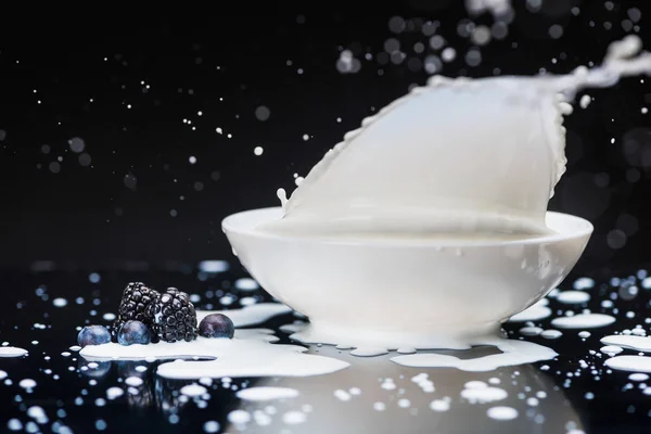 Salpicar leche con bayas crudas en un tazón blanco sobre fondo negro - foto de stock