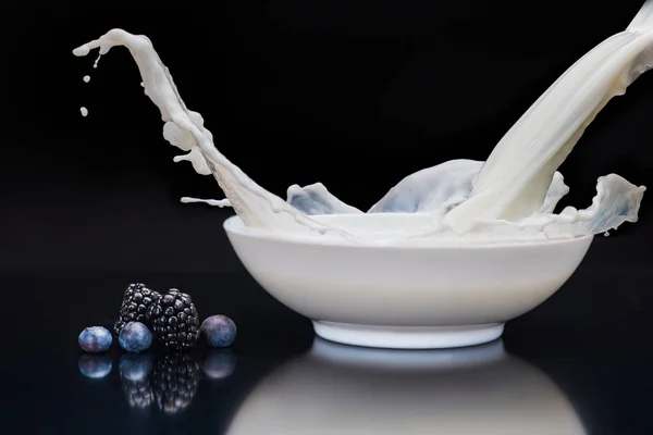 Mûres et bleuets par bol blanc avec verser du lait sur fond noir — Photo de stock