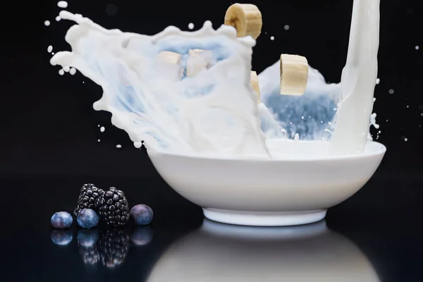 Pezzi di banana spruzzi in ciotola bianca con latte su sfondo nero — Foto stock