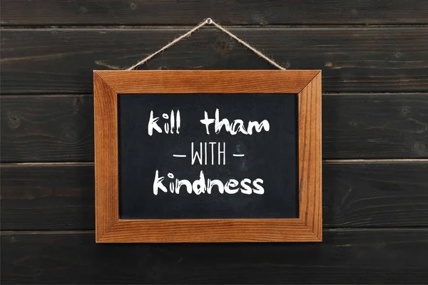 Blackboard with kill tham with kindness inscription hanging on wooden wall — Stock Photo