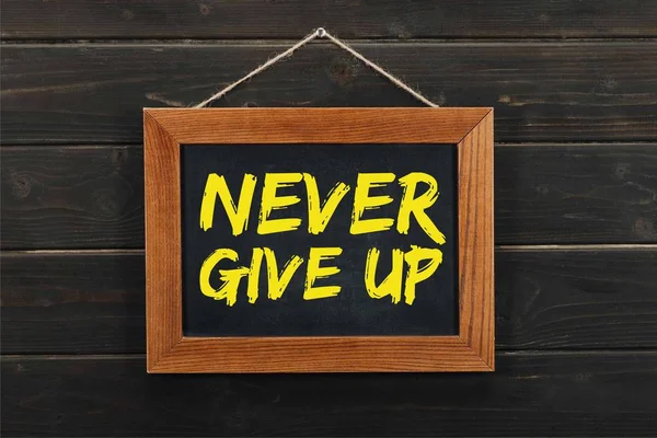 Blackboard with inscription never give up hanging on wooden wall — Stock Photo