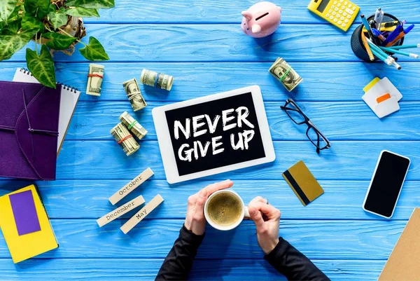 Hands holding coffee cup on blue wooden table by money and digital tablet, Never give up inspiration — Stock Photo