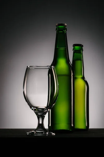 Close up view of bottles of beer and empty glass on grey background — Stock Photo