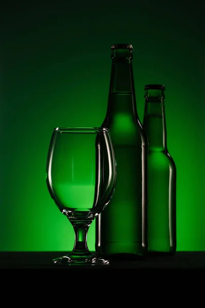 Vista de cerca de botellas de cerveza y vidrio vacío sobre fondo verde - foto de stock