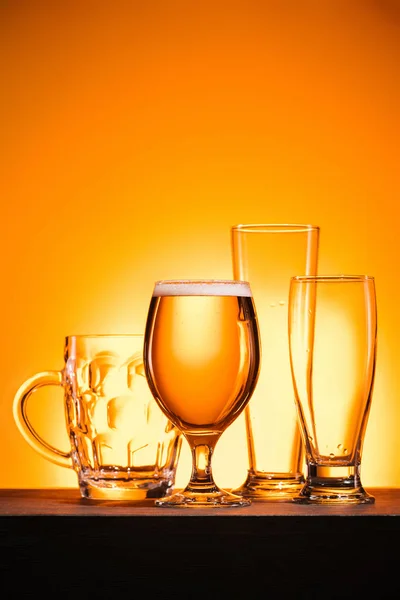 Vista de perto de copos vazios dispostos e caneca de cerveja no fundo laranja — Fotografia de Stock