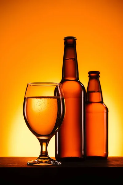 Vista ravvicinata di bottiglie e vetro di birra sulla superficie su sfondo arancione — Foto stock
