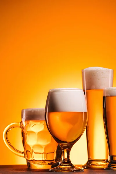 Vista ravvicinata di tazze disposte di birra fredda con schiuma su sfondo arancione — Foto stock