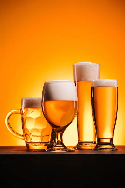 Close up view of arranged mugs of cold beer with froth on orange background — Stock Photo