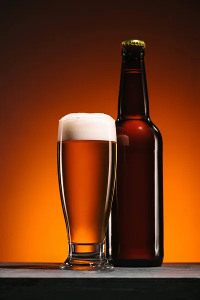 Close up view of bottle and mug of beer on orange backdrop — Stock Photo