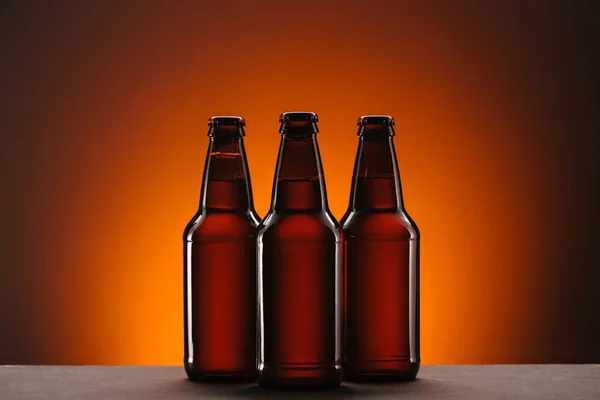 Vista de perto de garrafas arranjadas de cerveja em pano de fundo laranja — Fotografia de Stock