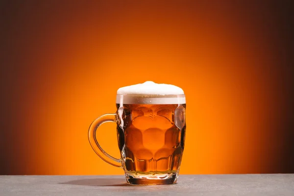 Nahaufnahme des Bechers mit kaltem Bier auf orangefarbenem Hintergrund — Stockfoto