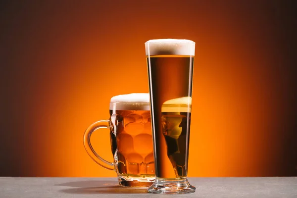 Крупный план расположения бокалов пива с пеной на оранжевом фоне — стоковое фото