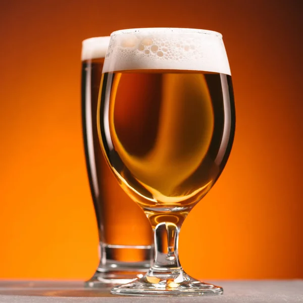 Selective focus of arrangement of glasses of beer with froth on orange backdrop — Stock Photo