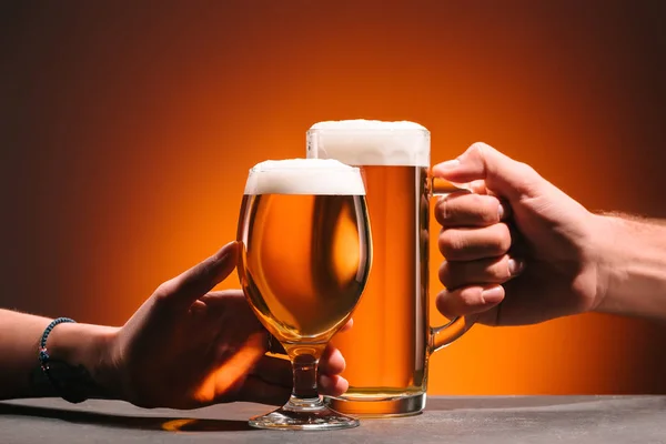 Partial view of people holding mugs on beer in hands on orange background — Stock Photo