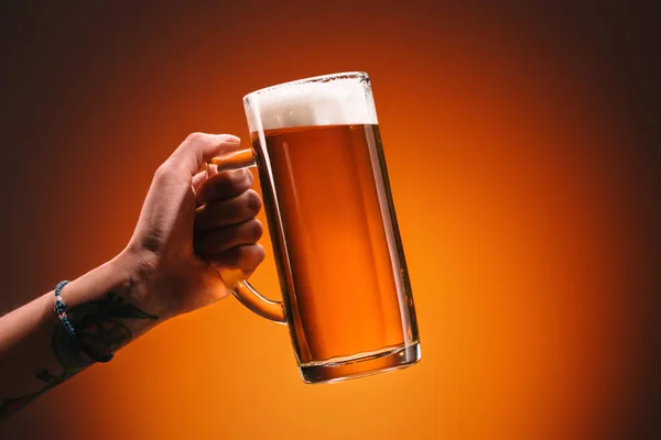 Cropped shot of woman holding glass of cold beer with foam on orange backdrop — Stock Photo