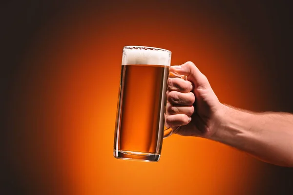 Recortado disparo de hombre sosteniendo taza de cerveza fría sobre fondo naranja - foto de stock