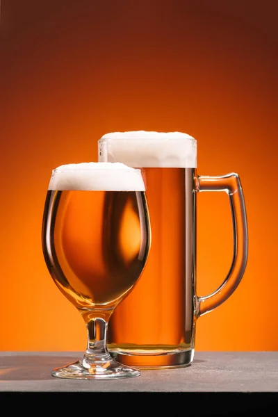 Close up view of arrangement of glasses of beer with foam on orange backdrop — Stock Photo