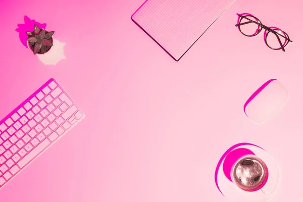 Pink toned picture of coffee cup, plant, eyeglasses, empty textbook, computer keyboard and mouse on table — Stock Photo