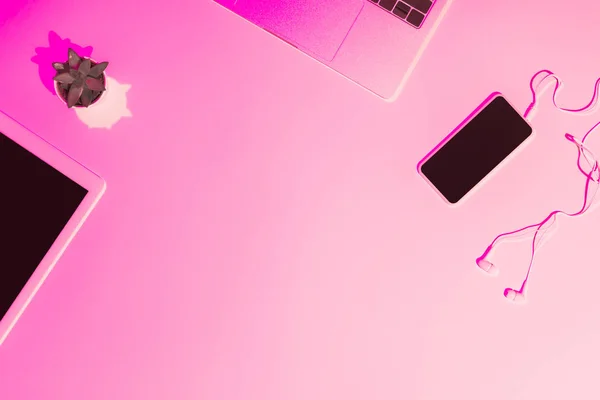 Pink toned picture of digital tablet, plant, laptop, smartphone and earphones on table — Stock Photo