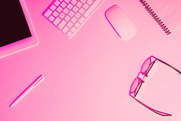 Розовое тонированное изображение пера, цифровой планшет, очки, учебник, клавиатура компьютера и мышь на столе — стоковое фото