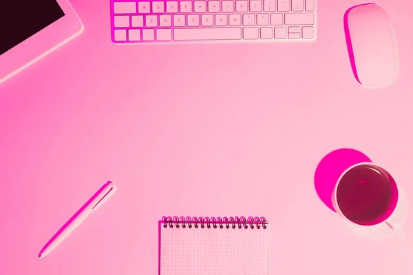 Pink toned picture of coffee cup, digital tablet, pen, textbook and computer keyboard on table — Stock Photo