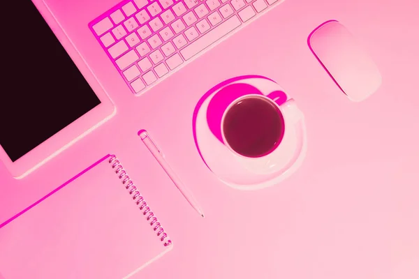 Pink toned picture of coffee cup, digital tablet, pen, textbook, computer keyboard and mouse on table — Stock Photo