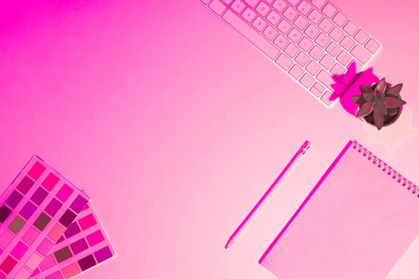 Cuadro tonificado rosa de pinturas, libro de texto vacío, lápiz, planta y teclado de ordenador en la mesa - foto de stock