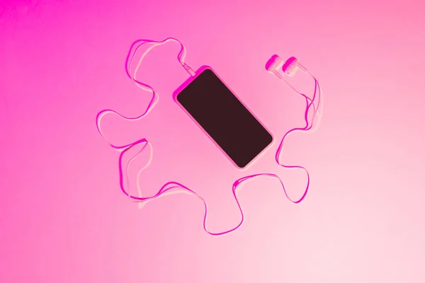 Pink toned picture of smartphone with earphones on pink background — Stock Photo