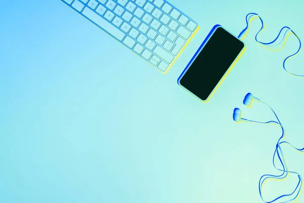 Blue toned picture of smartphone, earphones and computer keyboard — Stock Photo