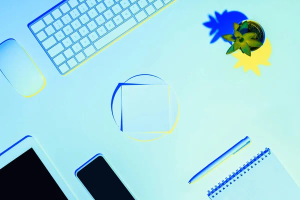 Blue toned picture of digital tablet, smartphone, computer keyboard and mouse, plant, textbook, pen and sticky note — Stock Photo