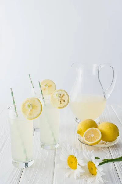 Close up view of lemonade in jug and glasses with straws on white wooden tabletop on grey background — Stock Photo