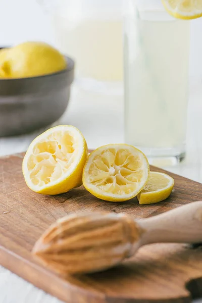 Close up view of lemon pieces and wooden squeezer on cutting board for making lemonade on white tabletop — Stock Photo